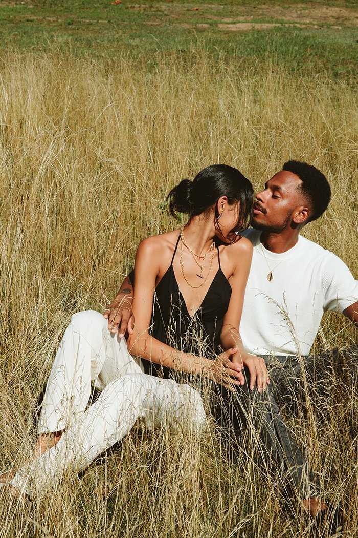 A couple in love, embracing one another while sitting outdoors surrounded by wild grass, modeling MEILI Gemstone Pillars 